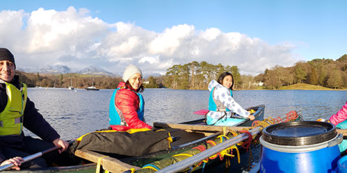 Malaysian family enjoying canoeing on coniston water with snowy mountains